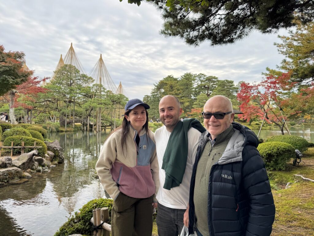 Tour guests at Kenrokuen Garden during a walking tour in Kanazawa, with seasonal trees and yukitsuri in the background.